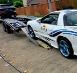 Two classic sports cars displayed side by side on pavement, featuring blue and white striping and racing livery