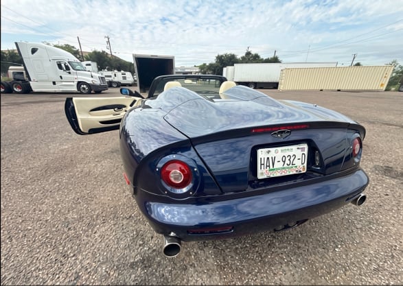 Dark blue Chevrolet Corvette in a parking lot with white RVs and trailers in the background.
