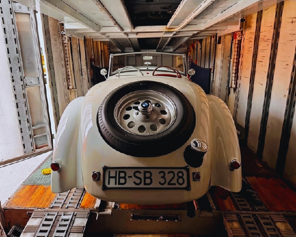 Vintage cream-colored Porsche 356 convertible with spare tire on trunk, parked in aircraft cargo hold