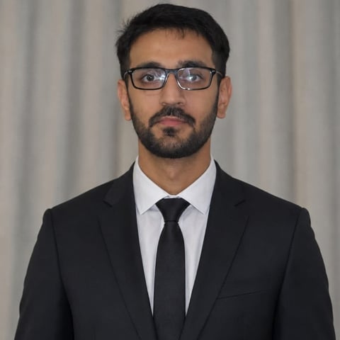 Professional headshot of a man wearing glasses, black suit, and black tie against a neutral gray background.