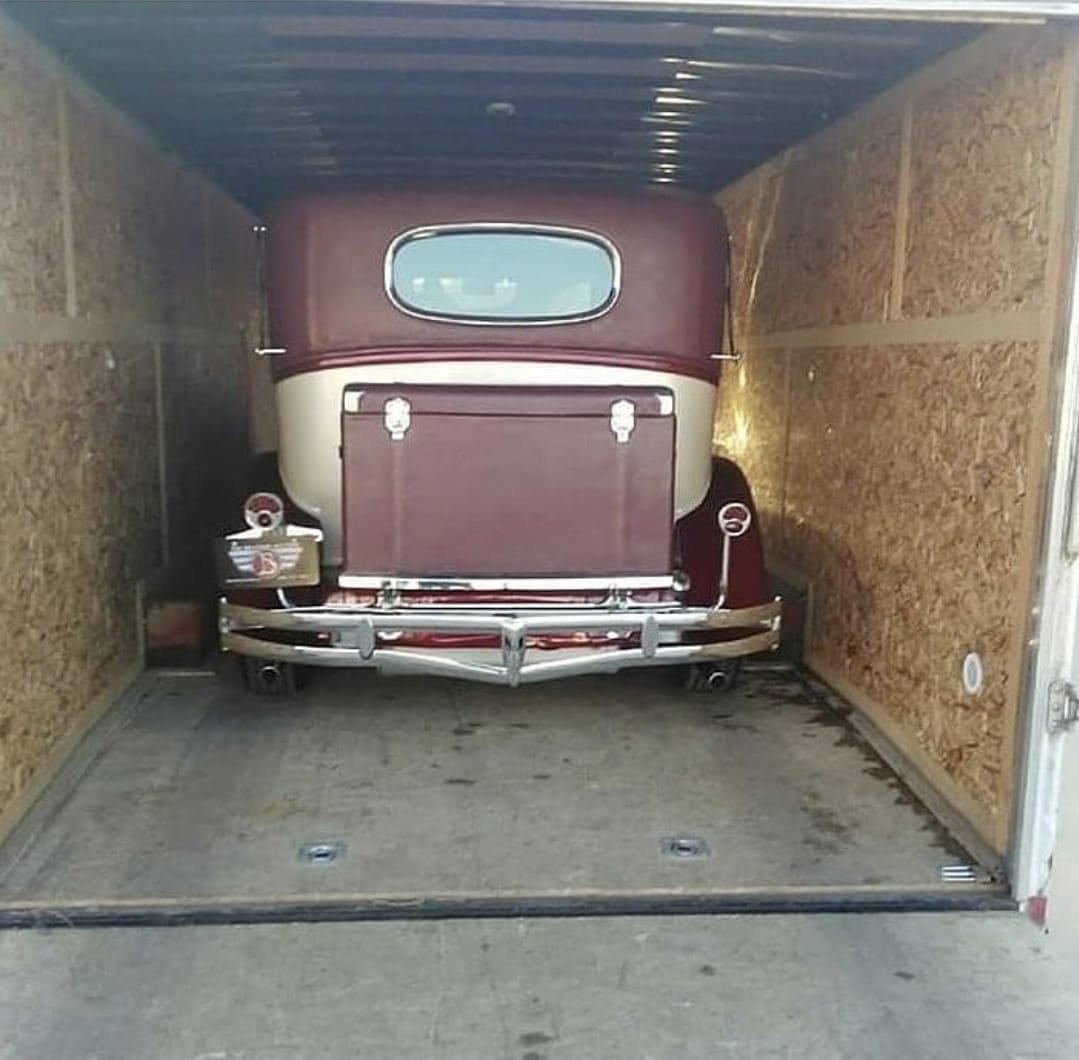Vintage maroon truck loaded in wooden-walled cargo trailer viewed from behind