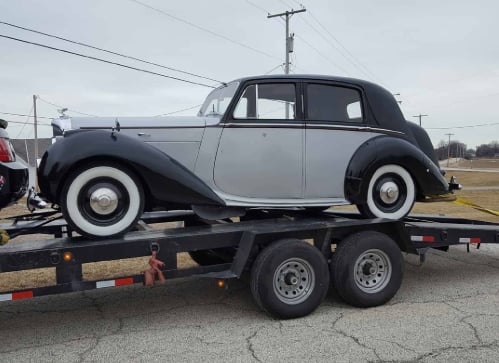 Vintage two-tone black and white sedan from the 1930s-40s era being transported on a flatbed trailer