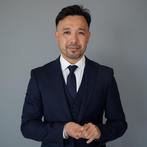 Professional headshot of a man in dark business suit and tie against gray background