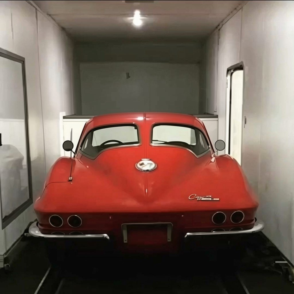 Red 1963 Chevrolet Corvette Stingray displayed in a white-walled garage, front view showing dual headlights and distinctive split rear window design