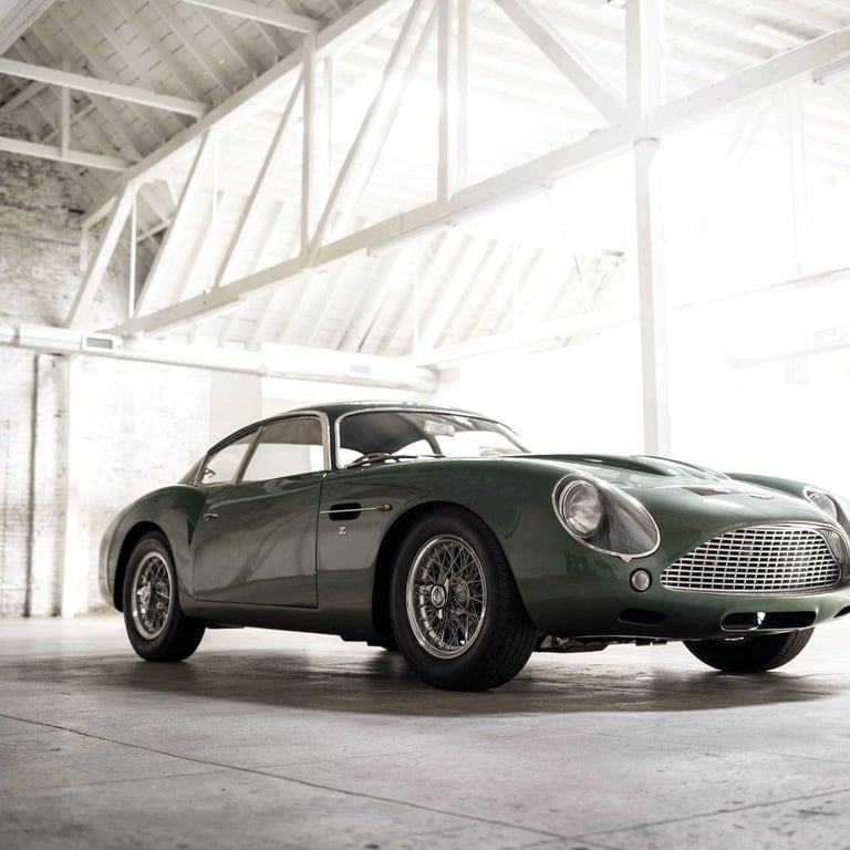 Vintage green sports car with white-wall tires parked in a modern warehouse with industrial ceiling beams