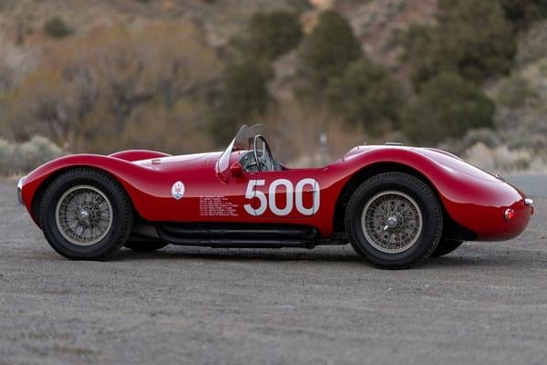 Red vintage race car number 500 with open cockpit, shown in profile view against a blurred mountainous background