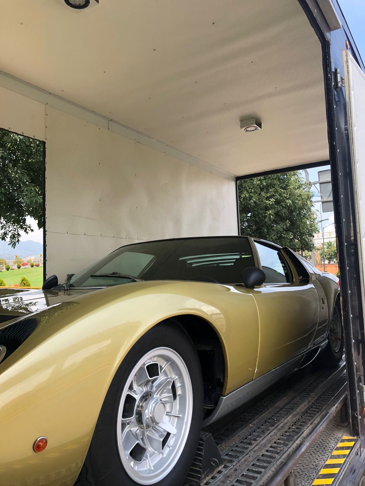 Yellow sports car loaded in enclosed white cargo trailer with open door and rural landscape visible