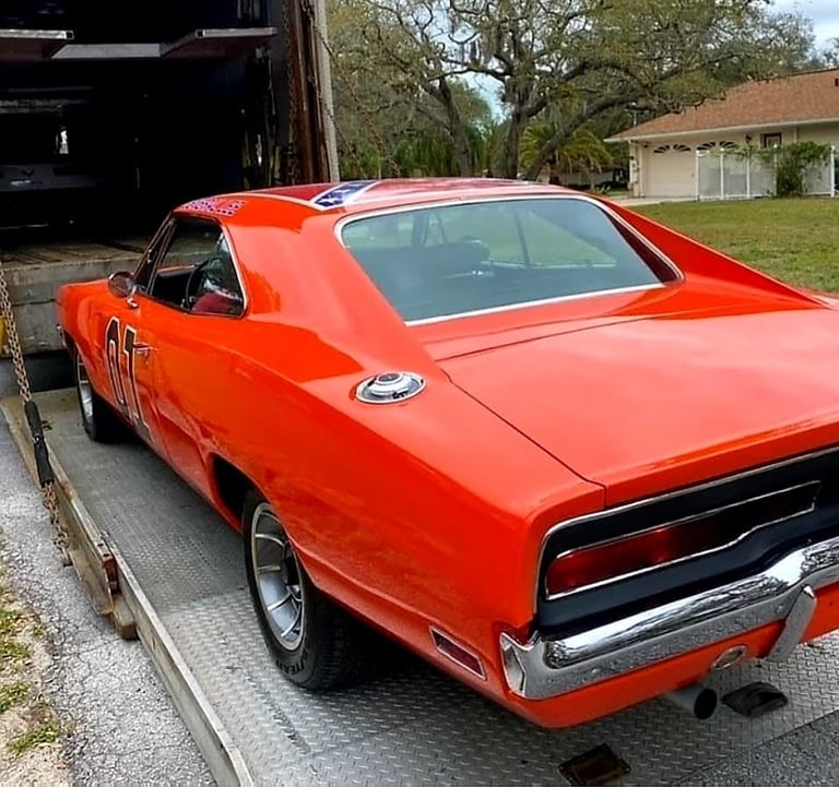 Bright red vintage muscle car on a flatbed trailer in a residential driveway