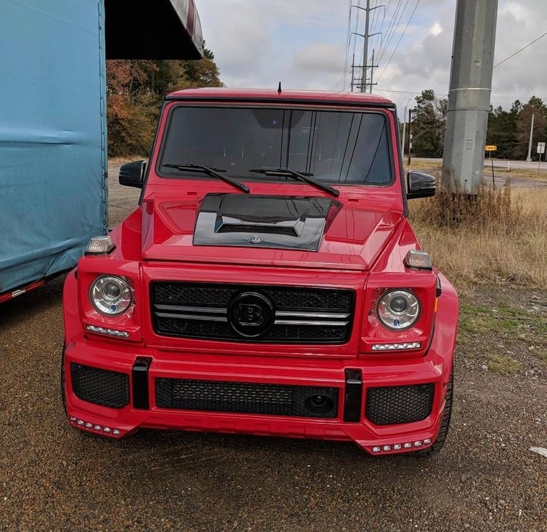 Red Mercedes-Benz G-Class SUV with custom front bumper parked on gravel near utility pole