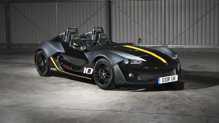 Black open-cockpit sports car with yellow accents and number 10 badging in an industrial garage setting