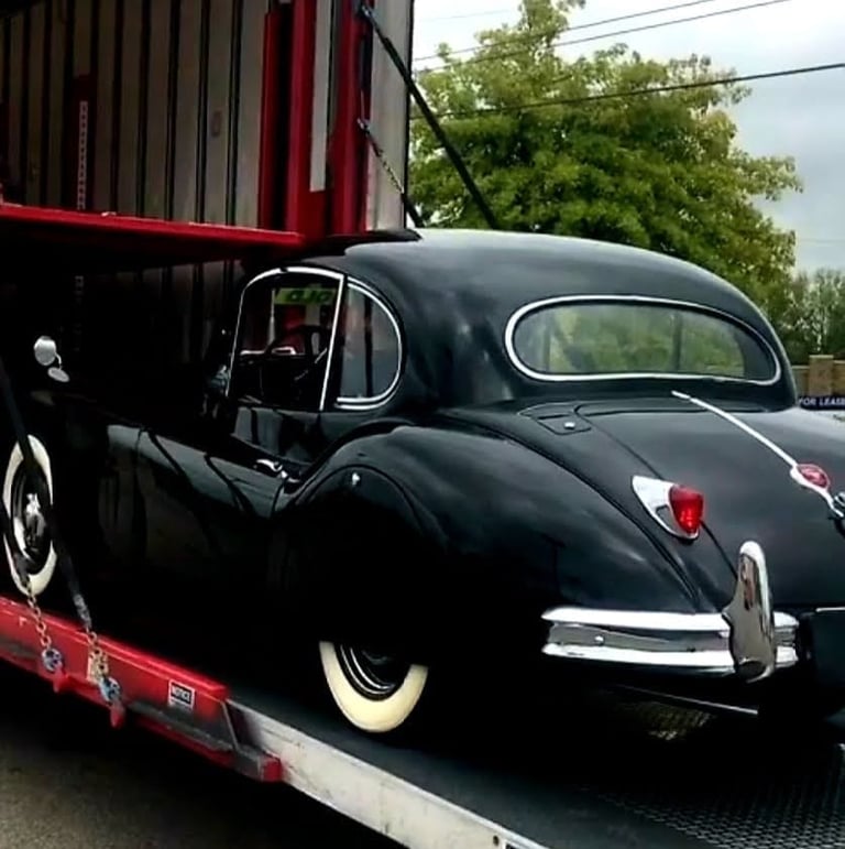 Vintage black Beetle car with white-wall tires being transported on a red flatbed trailer